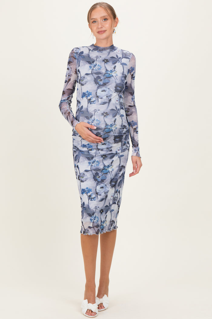 woman wearing a floral print long sleeve maternity dress, gently cradling her baby bump