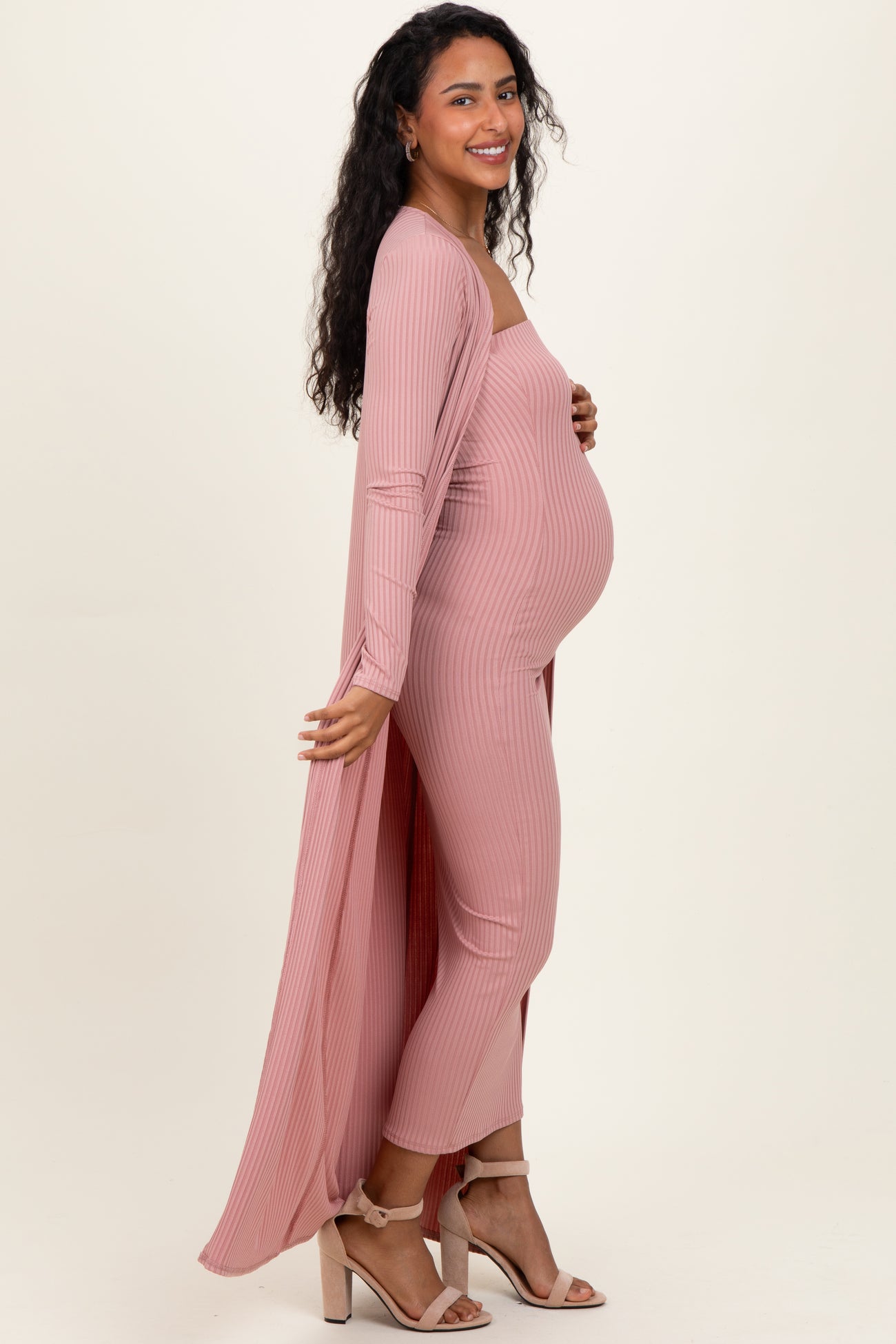 woman wearing a light pink maternity jumpsuit with a long cardigan, showcasing her baby bump