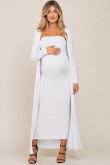 woman wearing a white ribbed maternity dress with a matching long cardigan and holding her baby bump