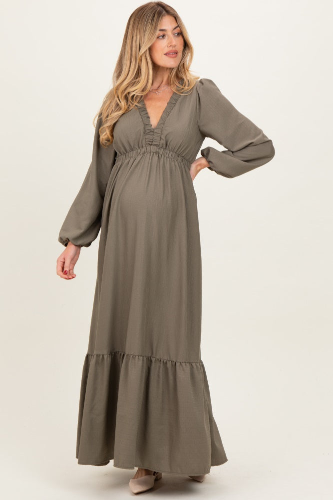 woman wearing a khaki long sleeve maternity maxi dress with a ruffled neckline and a flowing skirt, displaying a baby bump