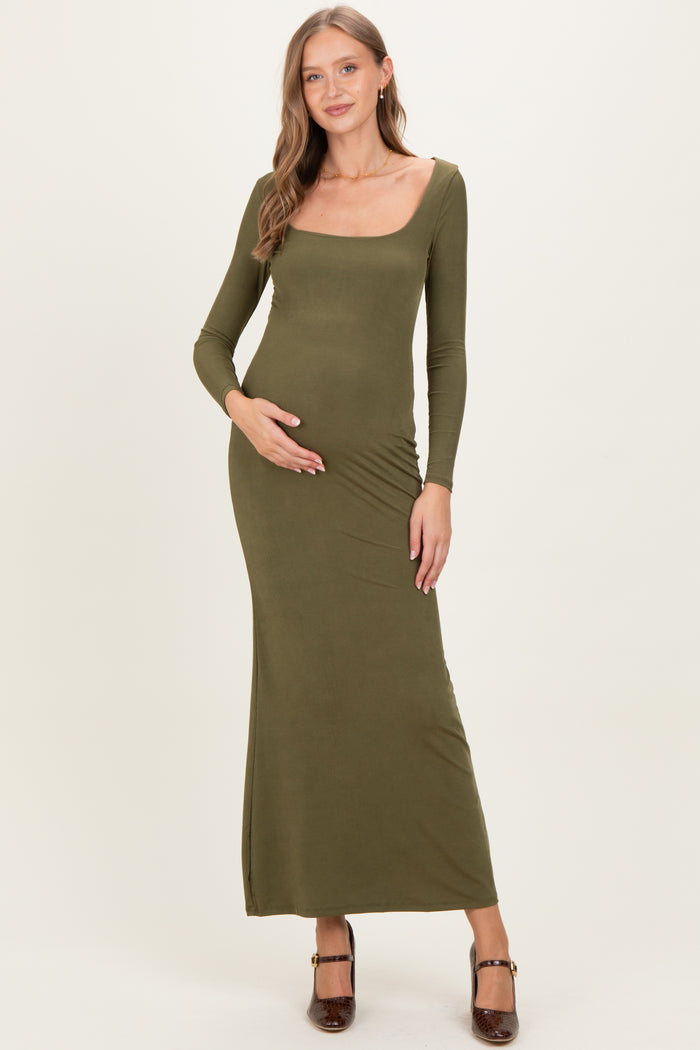 woman wearing a dark olive green long sleeve maternity dress, gently holding her baby bump