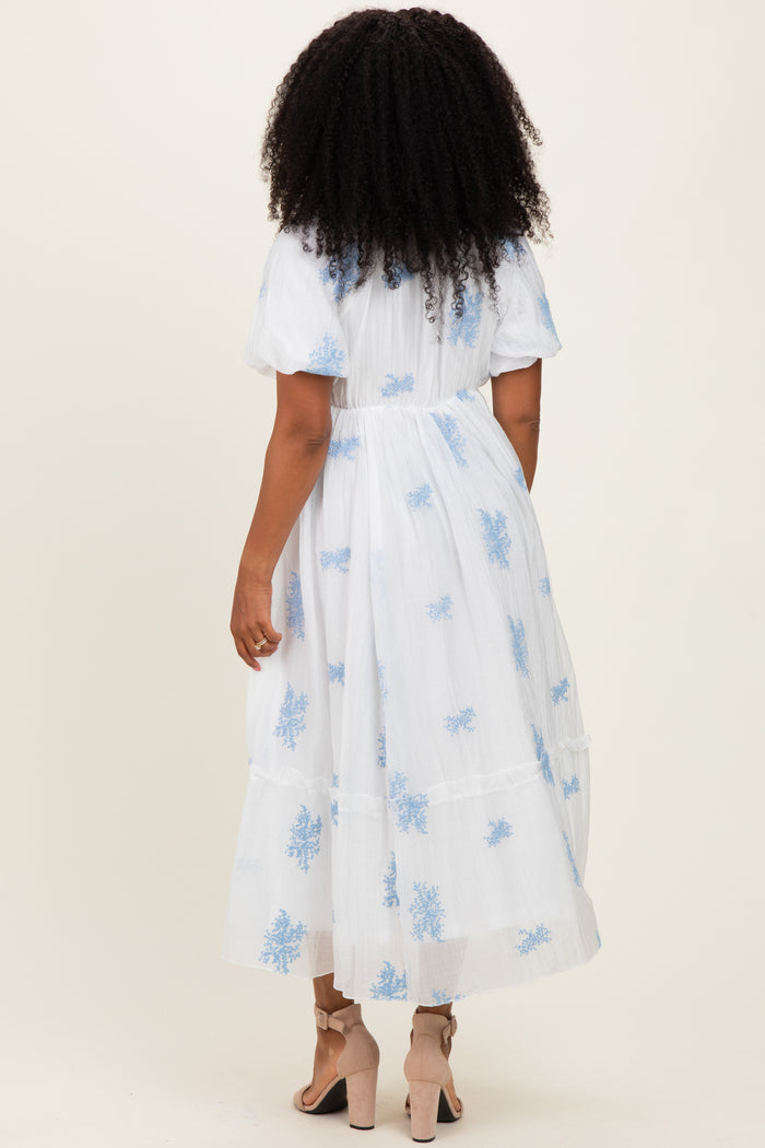 woman wearing a white midi dress with blue floral embroidery and puff sleeves, seen from the back