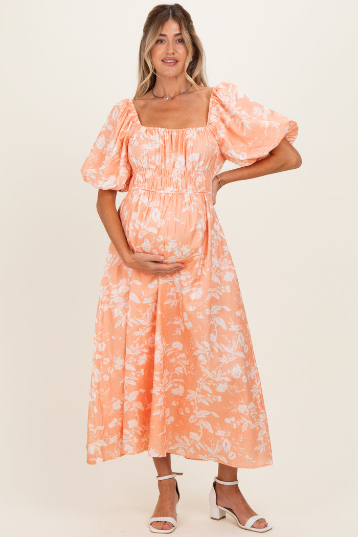 woman wearing a peach floral maternity dress with puff sleeves and holding her baby bump