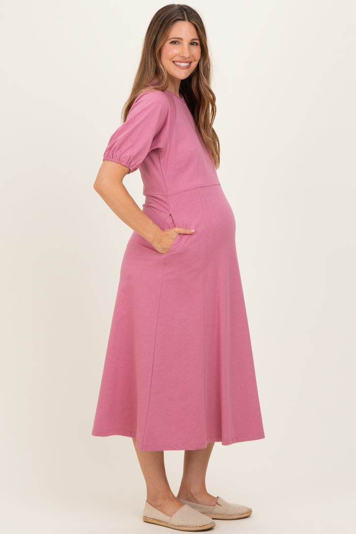 woman wearing a pink maternity dress with short puff sleeves and pockets, showing her baby bump
