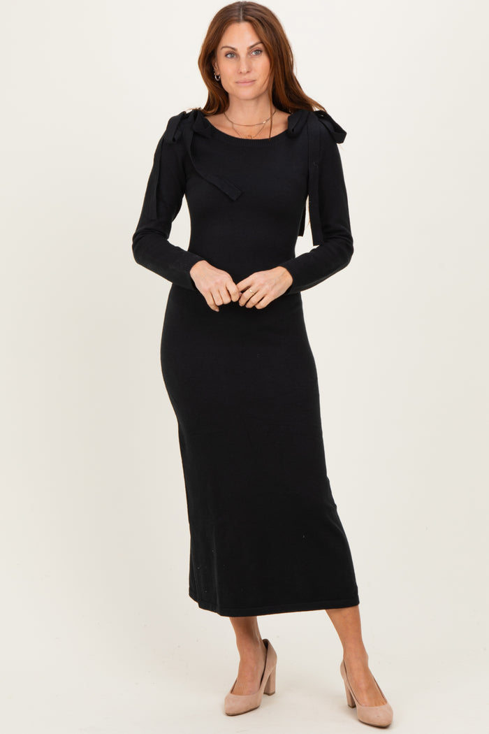 woman wearing a black long sleeve midi dress with bow details on the shoulders and nude heels