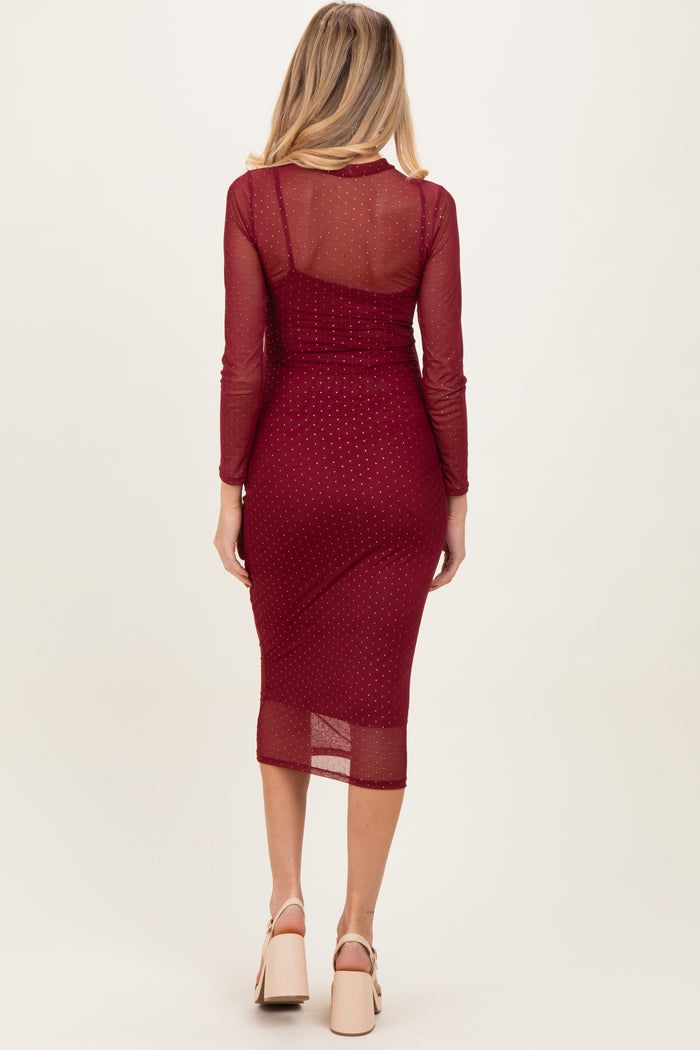 woman wearing a burgundy maternity midi dress with long sleeves and sheer back, showcasing her baby bump