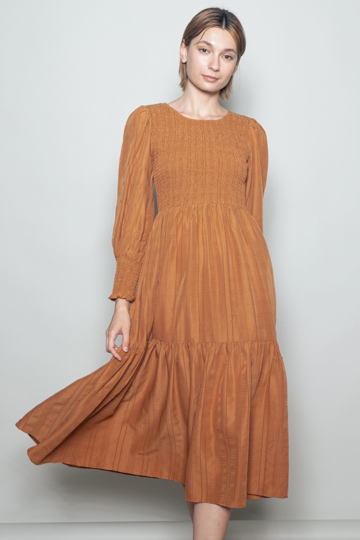 woman wearing a rust-colored long sleeve smocked midi dress with a tiered skirt and flowing fit