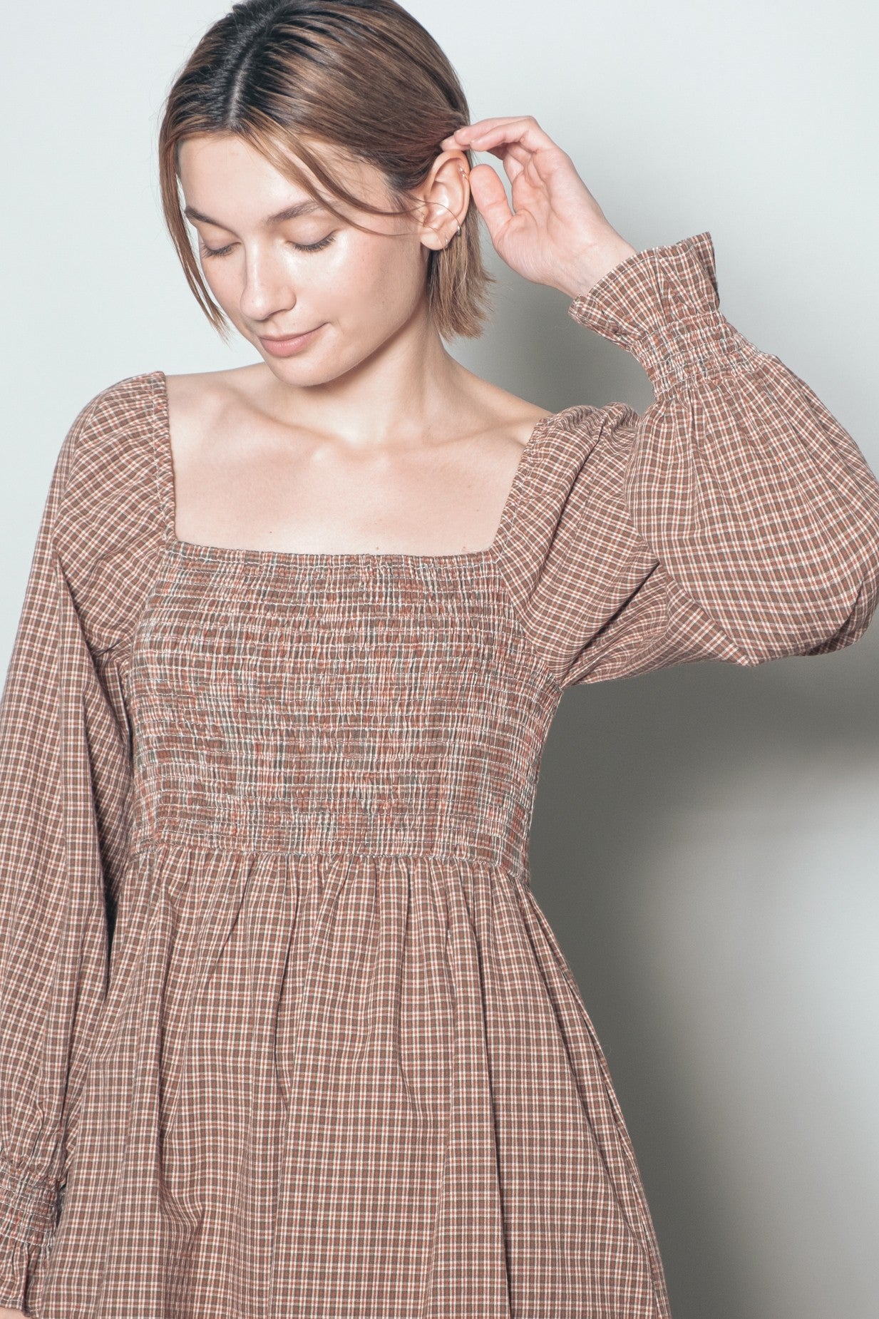 woman wearing a brown checkered smocked dress with long sleeves and a square neckline