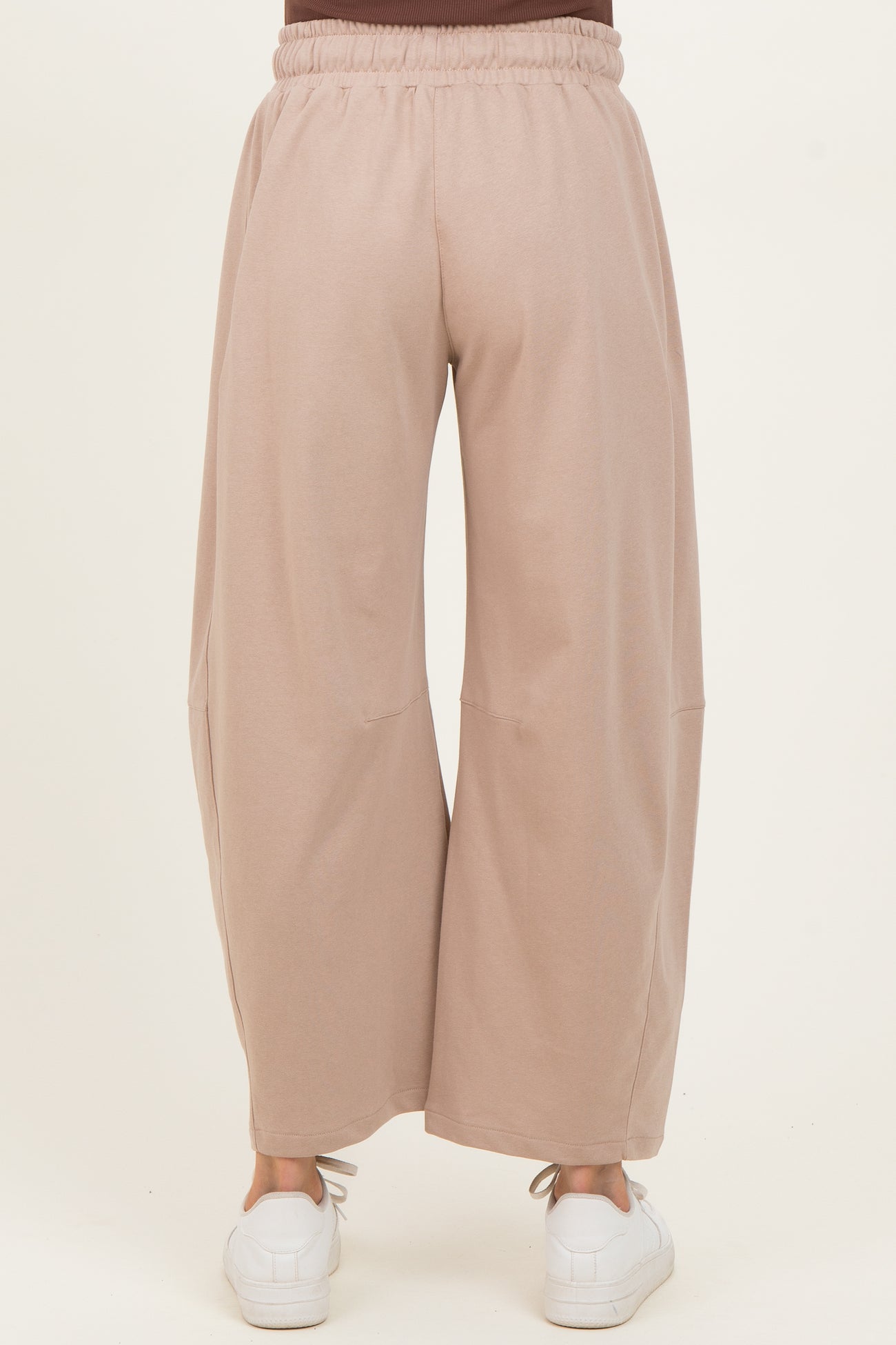 woman wearing light brown maternity wide-leg pants, viewed from the back with an elastic waistband and casual white sneakers