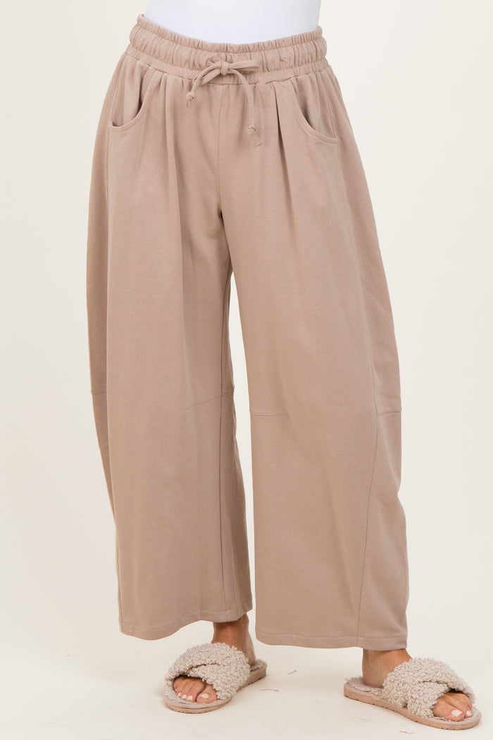 woman wearing light brown wide-leg lounge pants with side pockets and an elastic waist, paired with cozy slippers