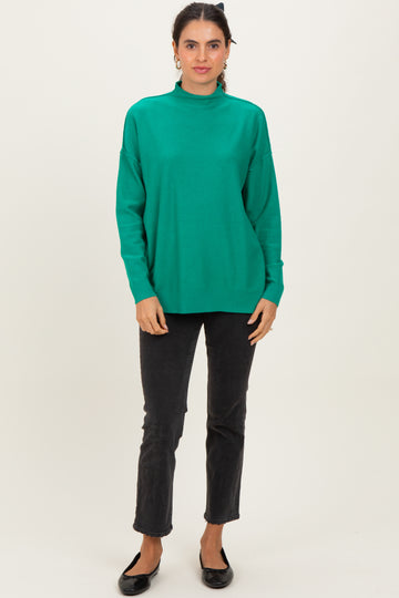 woman wearing a green turtleneck sweater and black cropped jeans, standing with hands at her sides