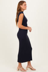 woman wearing a navy sleeveless ribbed maxi dress, standing sideways, paired with light-colored block-heeled sandals
