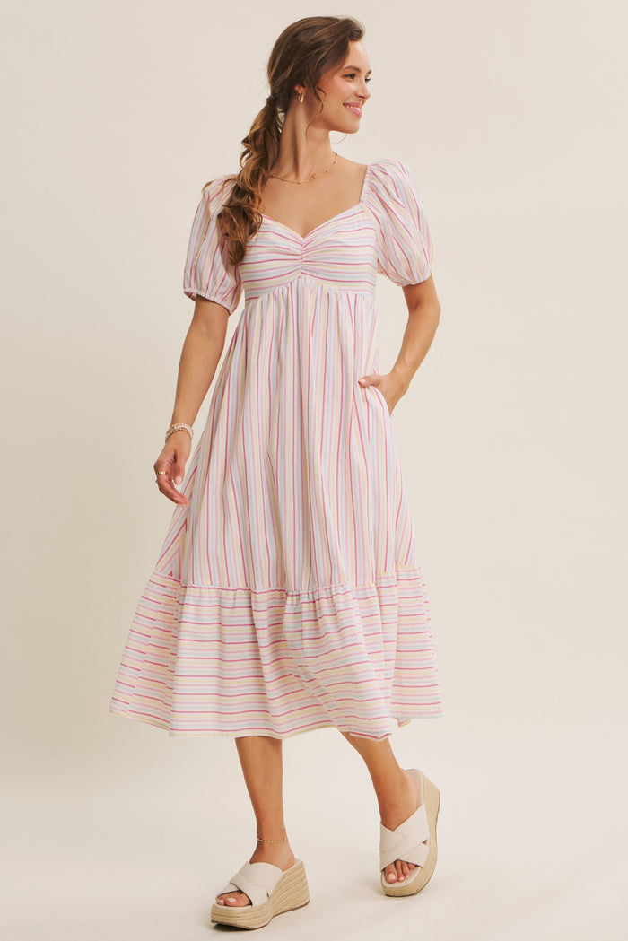 woman wearing a pink and white striped midi dress with puff sleeves and a tiered hem, standing in a relaxed pose