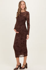 woman wearing a brown maternity dress with floral lace overlay and long sleeves, gently cradling her baby bump