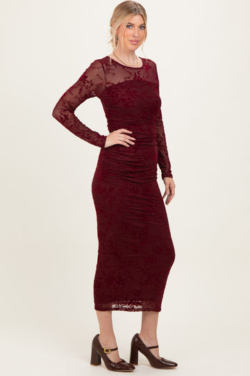 woman wearing a burgundy long sleeve midi dress with ruched details and floral lace overlay