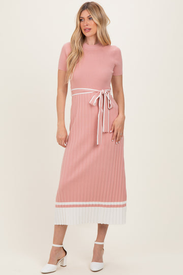 woman wearing a ribbed pink maxi dress with a white tie waist and striped hemline, styled with white heels