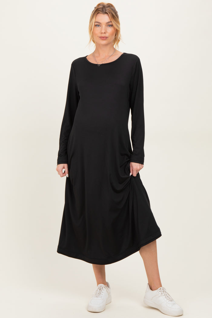 woman wearing a black long sleeve maternity dress with side pockets and a relaxed fit, showing her baby bump