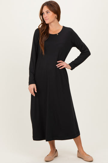 woman wearing a black long sleeve maxi dress, standing with one hand on her hip and a relaxed expression