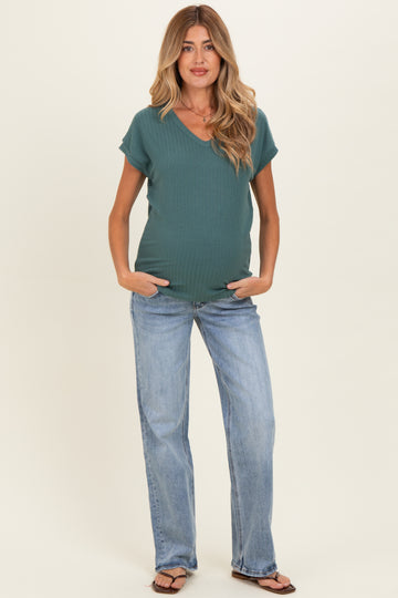 woman wearing a teal v-neck maternity top and light blue jeans, showing a baby bump