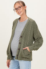 woman wearing an olive green textured maternity cardigan over a gray top, hands in pockets, showcasing a baby bump