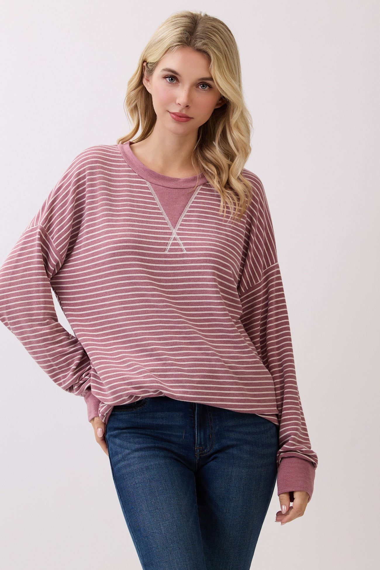 woman wearing a mauve striped long sleeve oversized sweatshirt with a v-neck and relaxed fit, paired with blue jeans