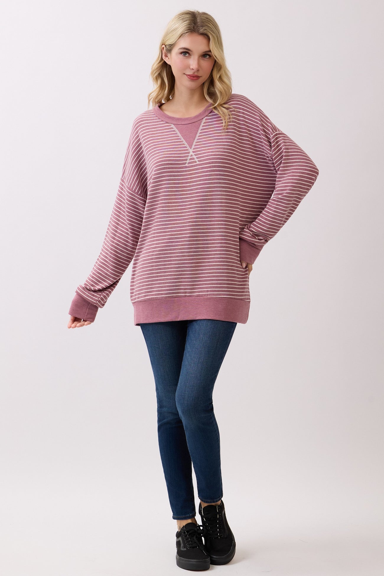 woman wearing a pink and white striped oversized sweatshirt with a v-neck and long sleeves, paired with blue jeans