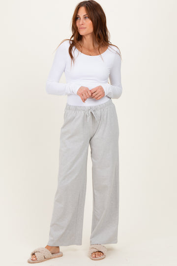 woman wearing a white long sleeve fitted top and light gray drawstring wide-leg pants, with cozy slippers