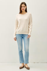 woman wearing a beige long sleeve sweater paired with light blue straight leg jeans and brown flats