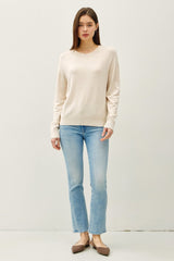 woman wearing a beige long sleeve sweater paired with light blue straight leg jeans and brown flats