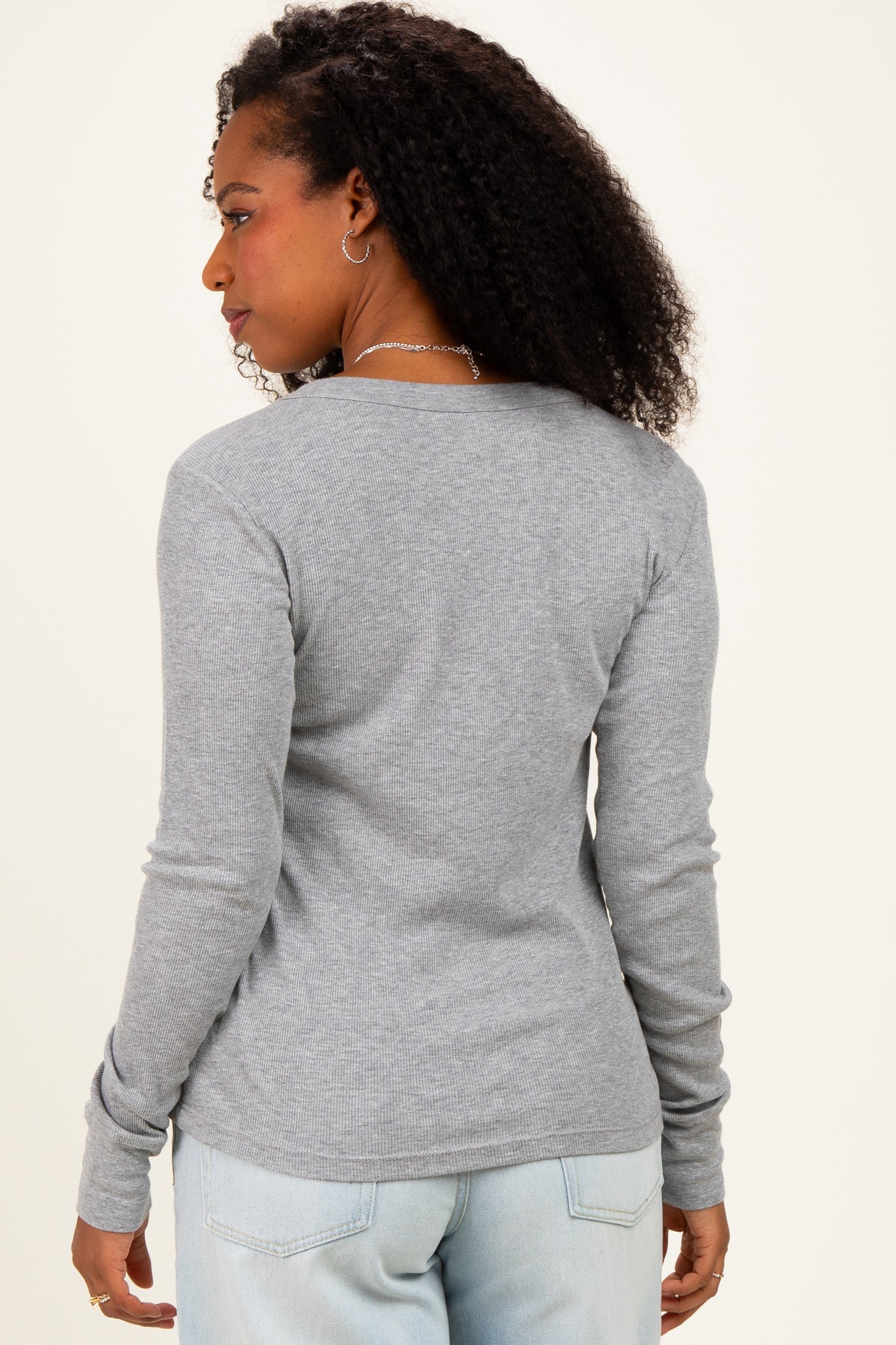 woman wearing a gray long sleeve ribbed top, viewed from the back with a relaxed fit and styled hair