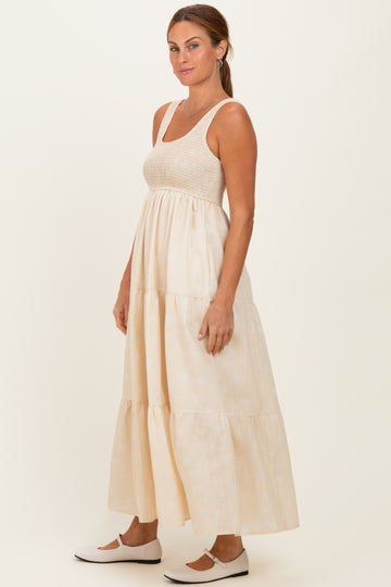 woman wearing a cream maxi dress with a tiered skirt and a fitted bodice, styled with white slip-on shoes