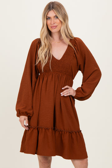 woman wearing a rust colored long sleeve dress with a deep v-neck and ruffle hemline