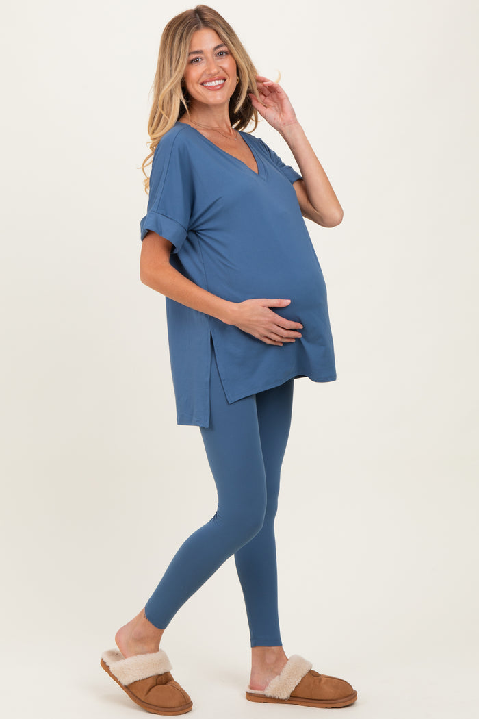 woman wearing a blue maternity top with a v-neck and rolled sleeves, holding her baby bump, paired with blue leggings