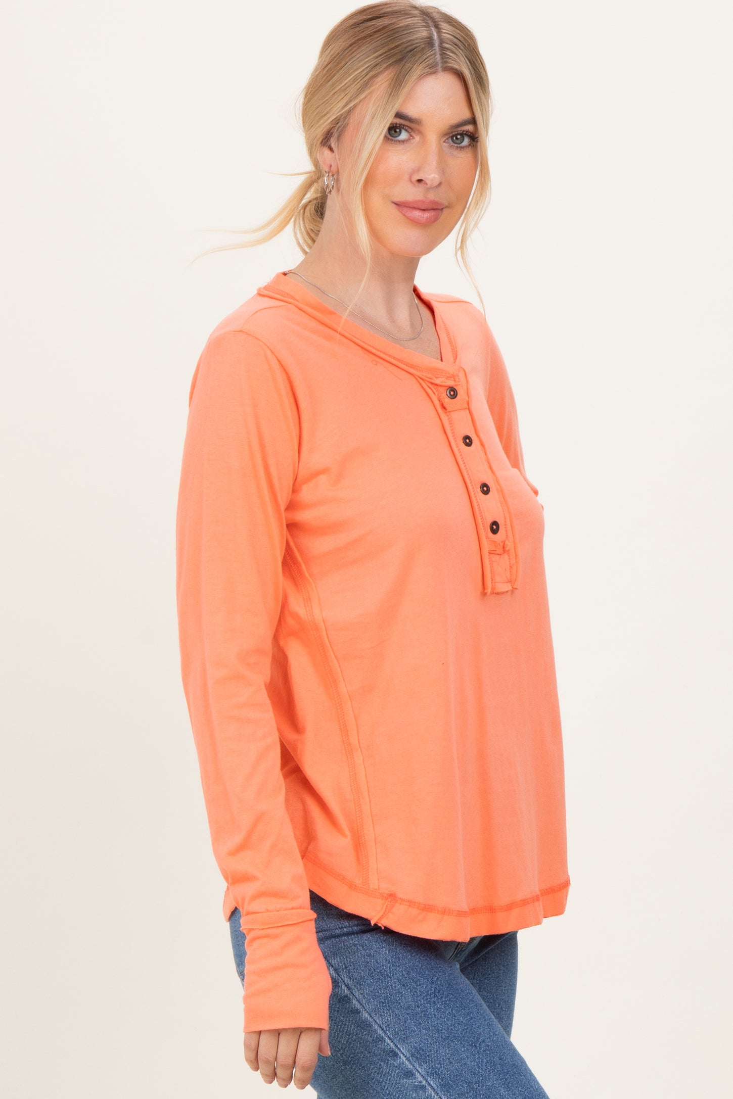 woman wearing a bright orange long sleeve henley top with button details and a relaxed fit