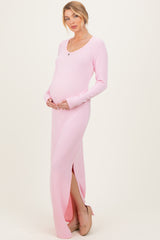 woman wearing a light pink ribbed maternity maxi dress with a side slit and holding her baby bump