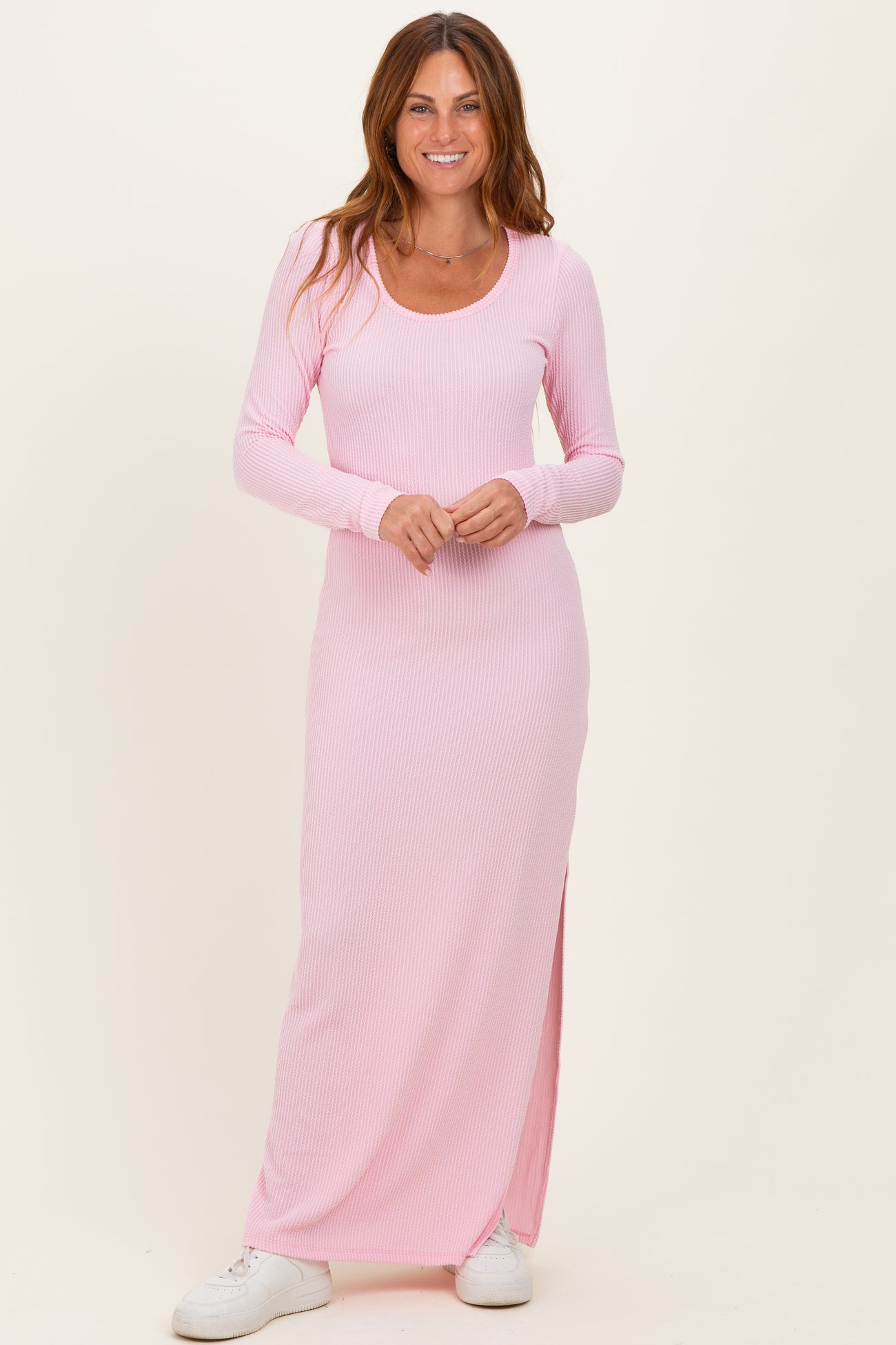 woman wearing a light pink long sleeve ribbed maxi dress with side slits and white sneakers