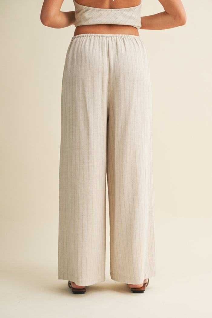 woman wearing beige high-waisted wide-leg pants with vertical stripes, viewed from the back