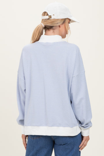 woman wearing a light blue striped long sleeve sweatshirt with a white trim and a white cap, viewed from the back