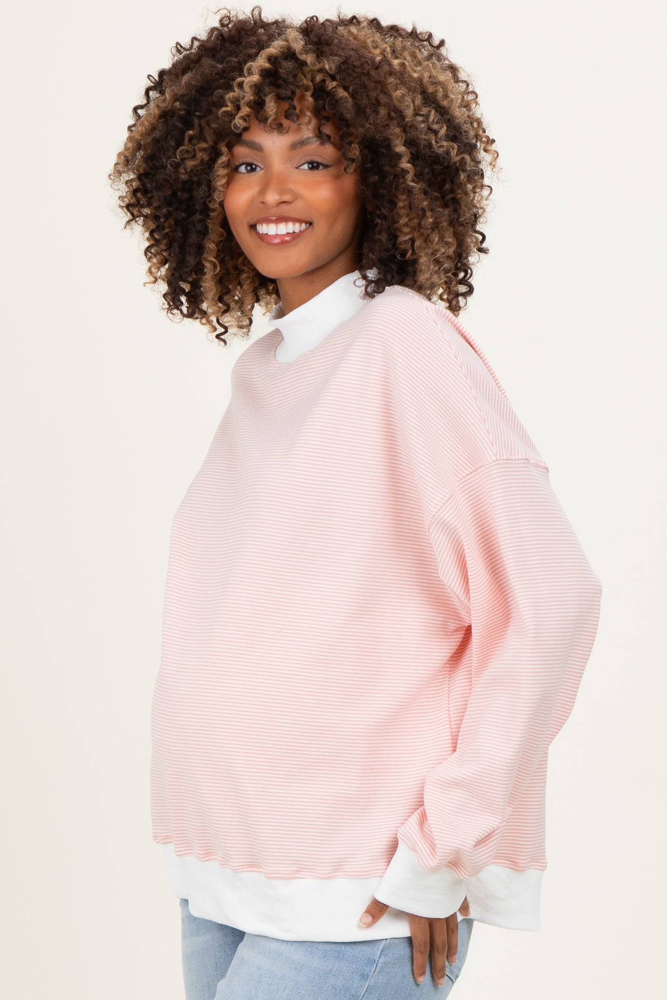 woman wearing a light pink striped maternity sweatshirt with a white collar and a visible baby bump