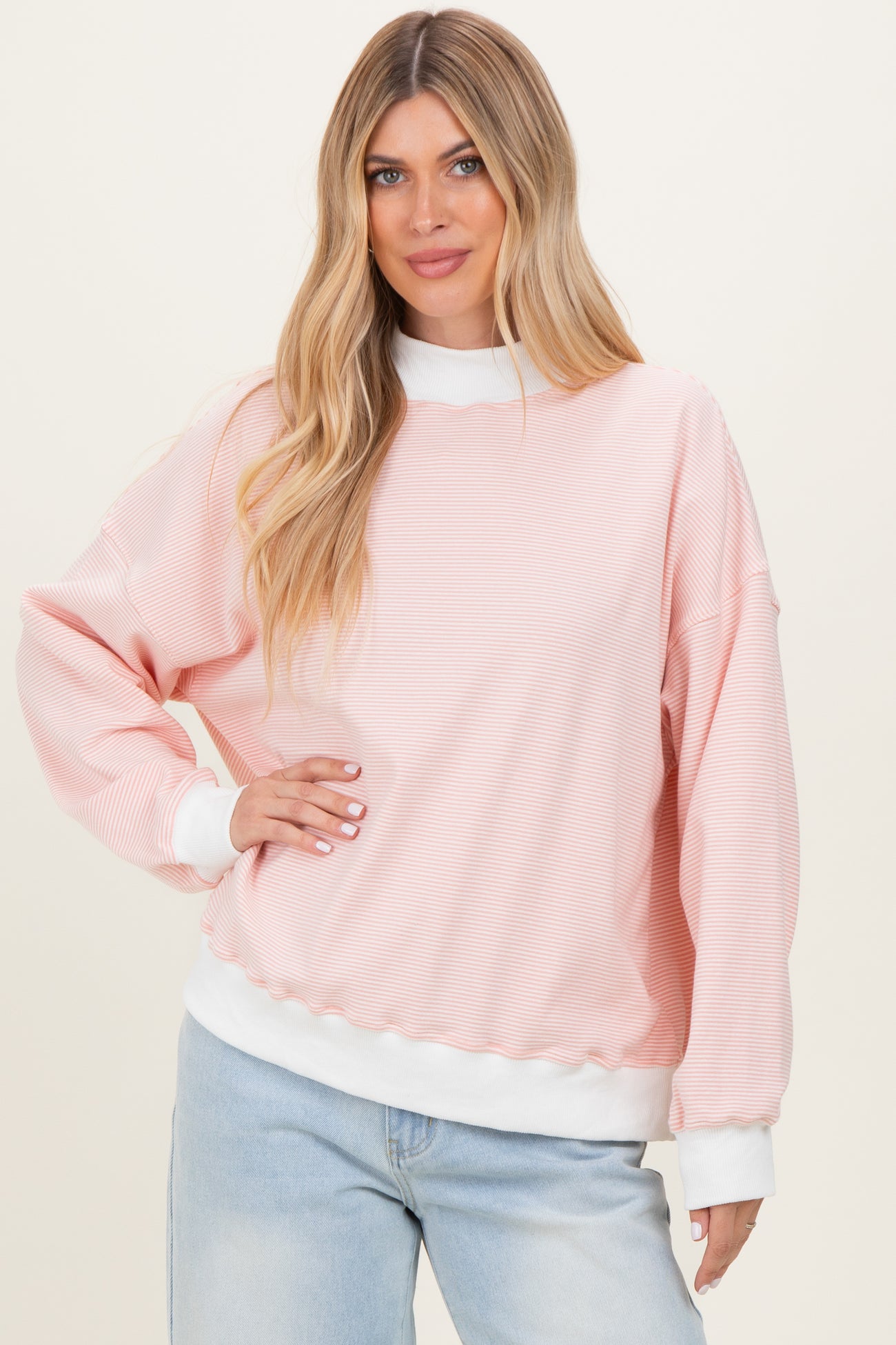 woman wearing a light pink striped oversized sweatshirt with white cuffs and hem, standing against a neutral background