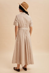 woman wearing a beige striped midi dress with a belted waist and short sleeves, standing with her back to the camera