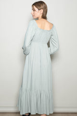 woman wearing a light green long sleeve maxi dress with a ruffled hem and an open back design