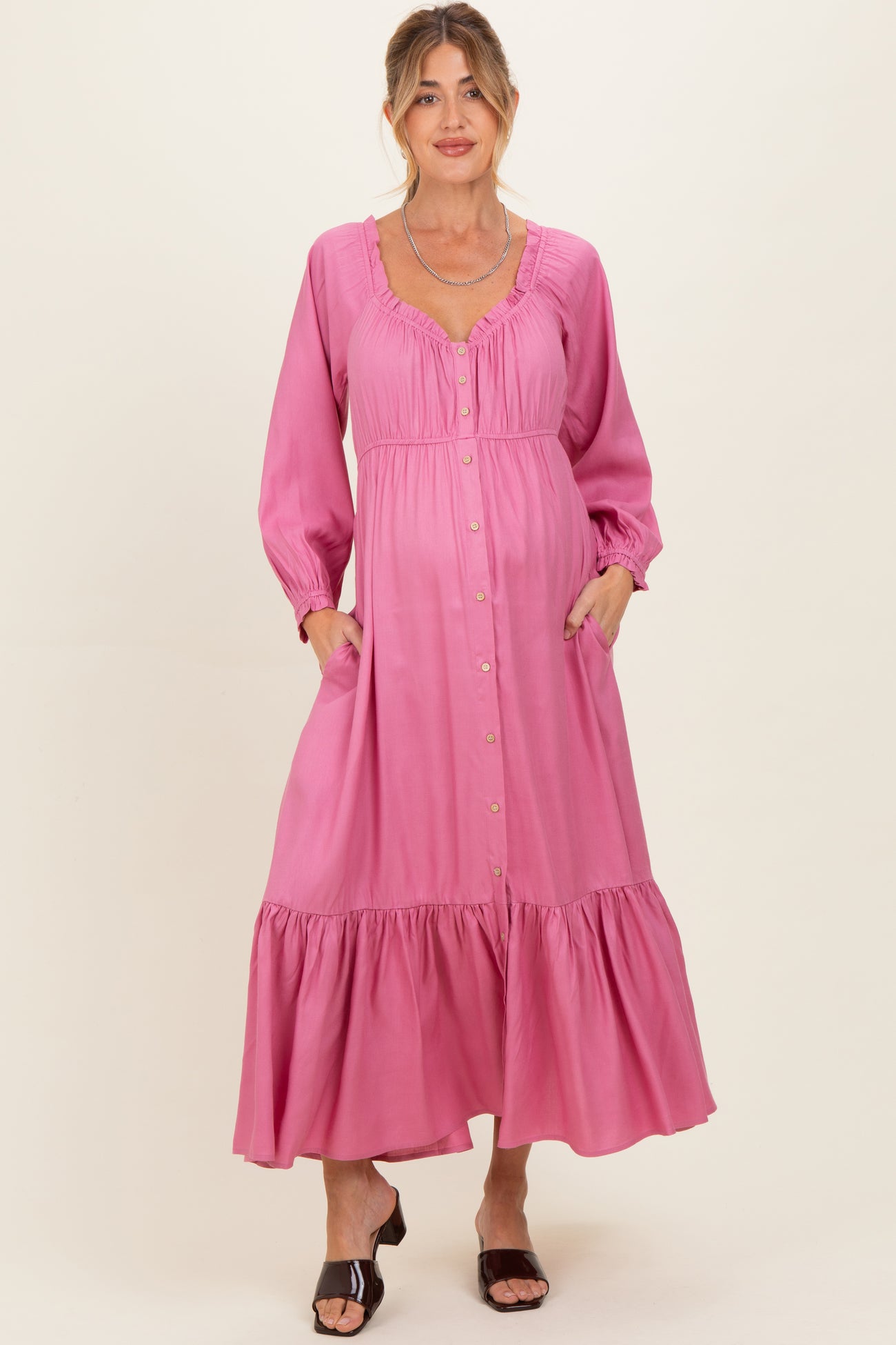 woman wearing a pink long sleeve maternity dress with buttons and pockets, featuring a tiered skirt and a baby bump