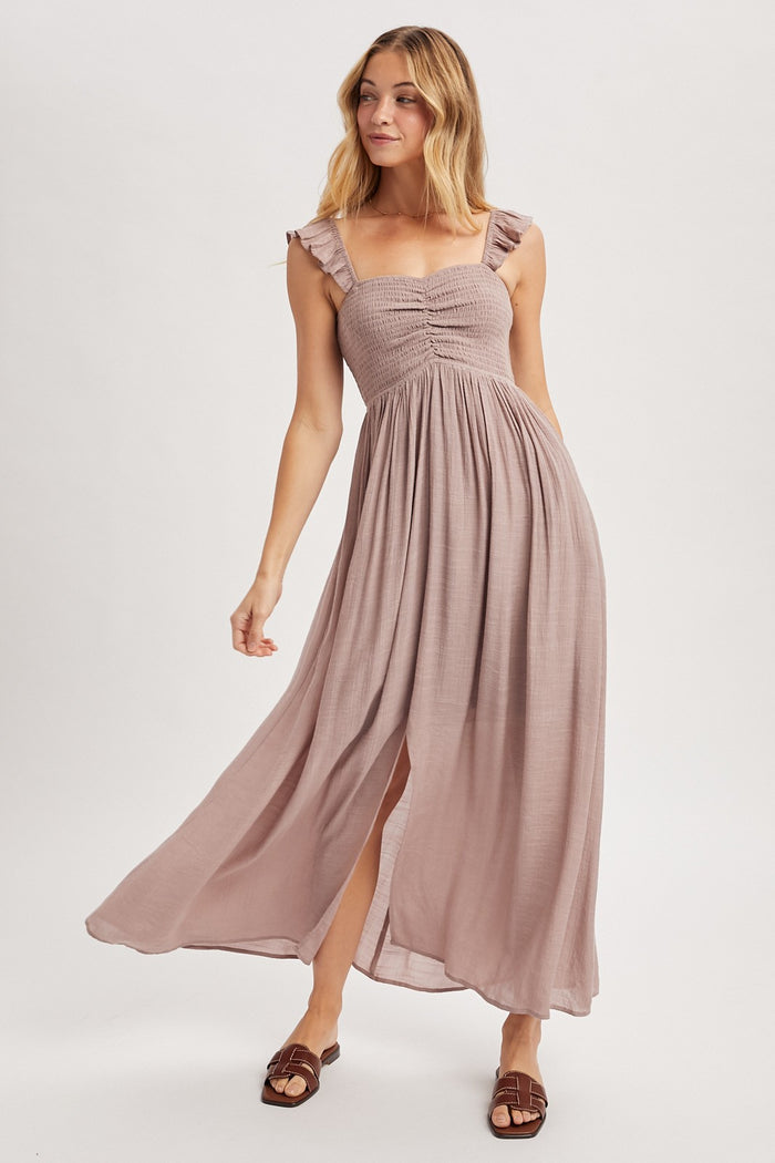 woman wearing a light mauve sleeveless maxi dress with ruffled straps and a front slit