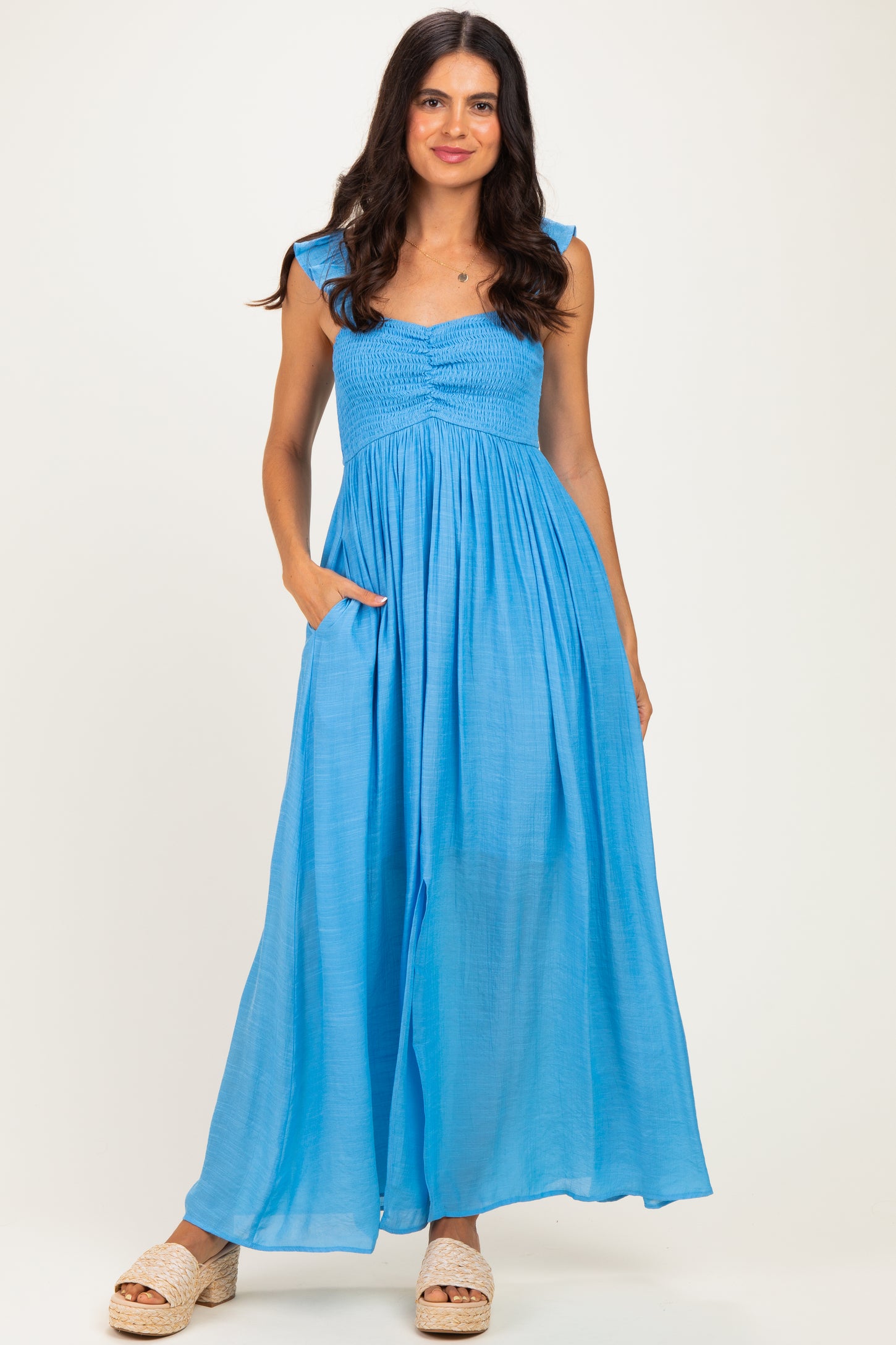 woman wearing a bright blue maxi dress with smocked bodice and shoulder straps, featuring side pockets