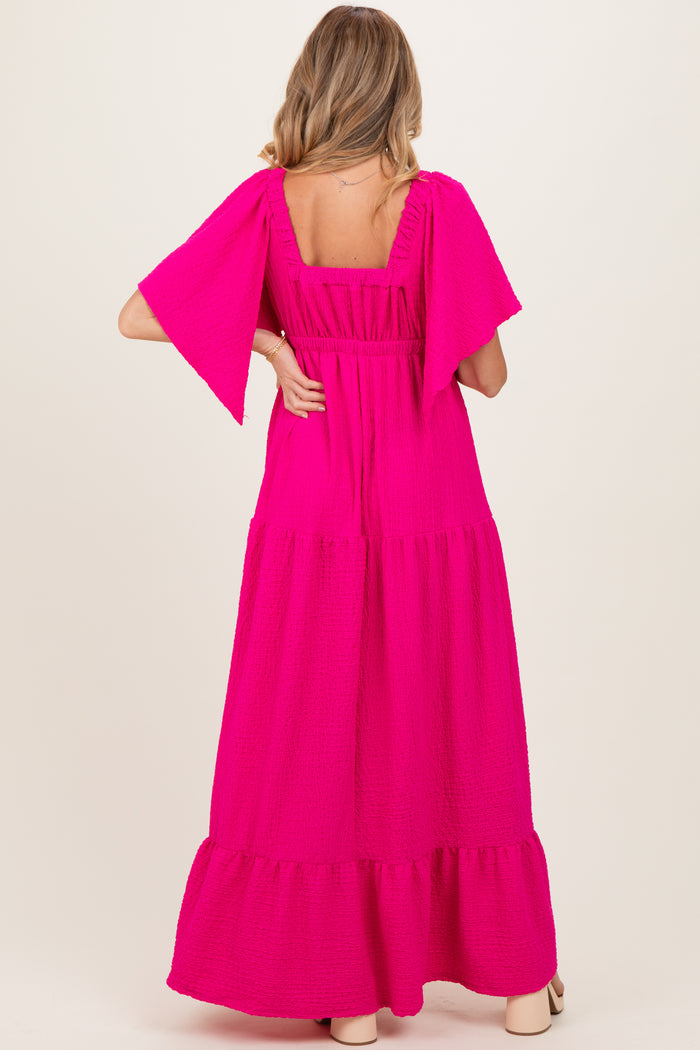woman wearing a flowing bright pink maternity maxi dress with flutter sleeves and a tiered skirt