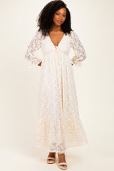 woman wearing a cream lace maxi dress with a deep V-neck and long sleeves, standing against a neutral background