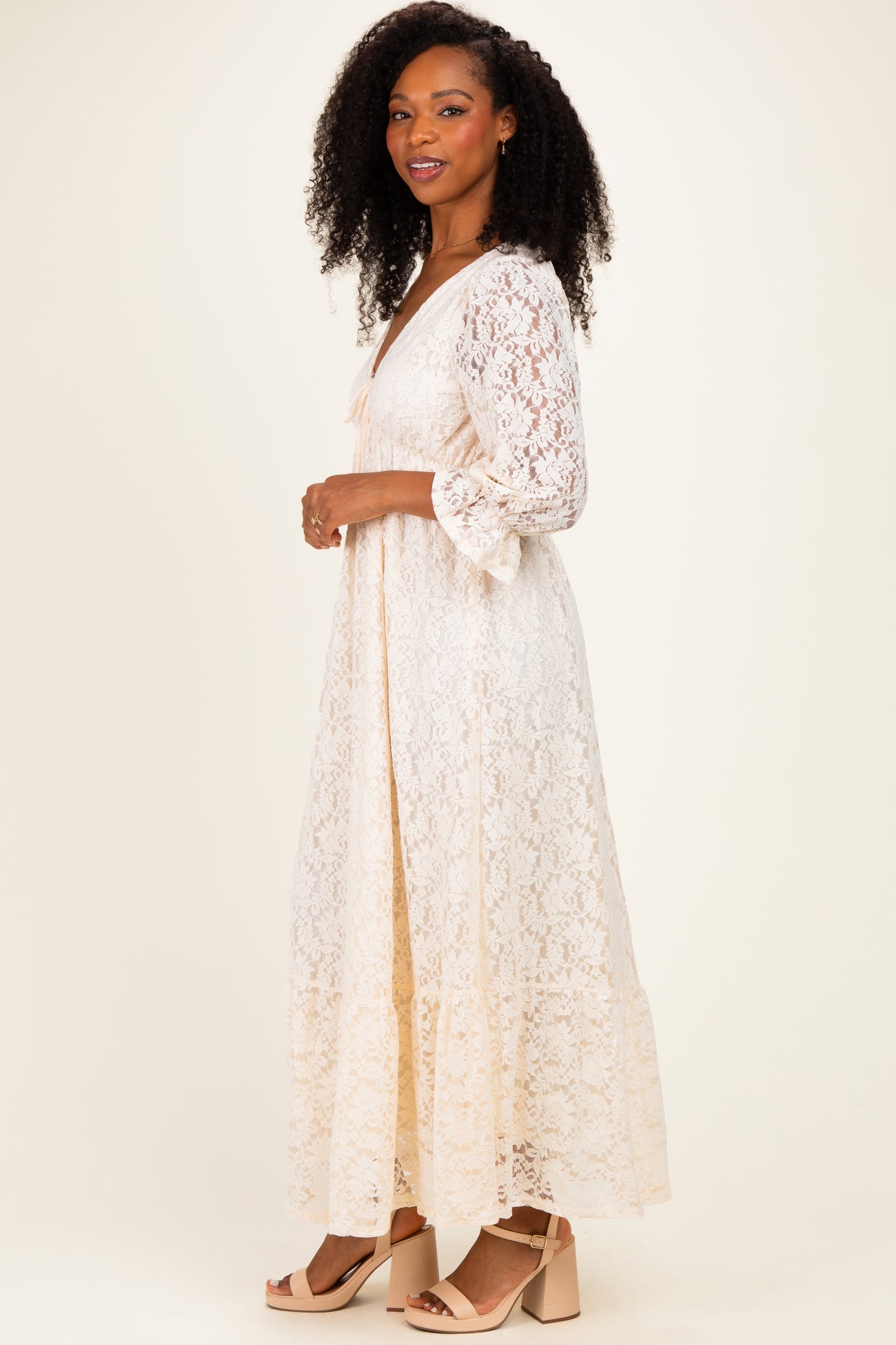 woman wearing a cream lace maxi dress with long sleeves and a v-neckline, styled with heeled sandals