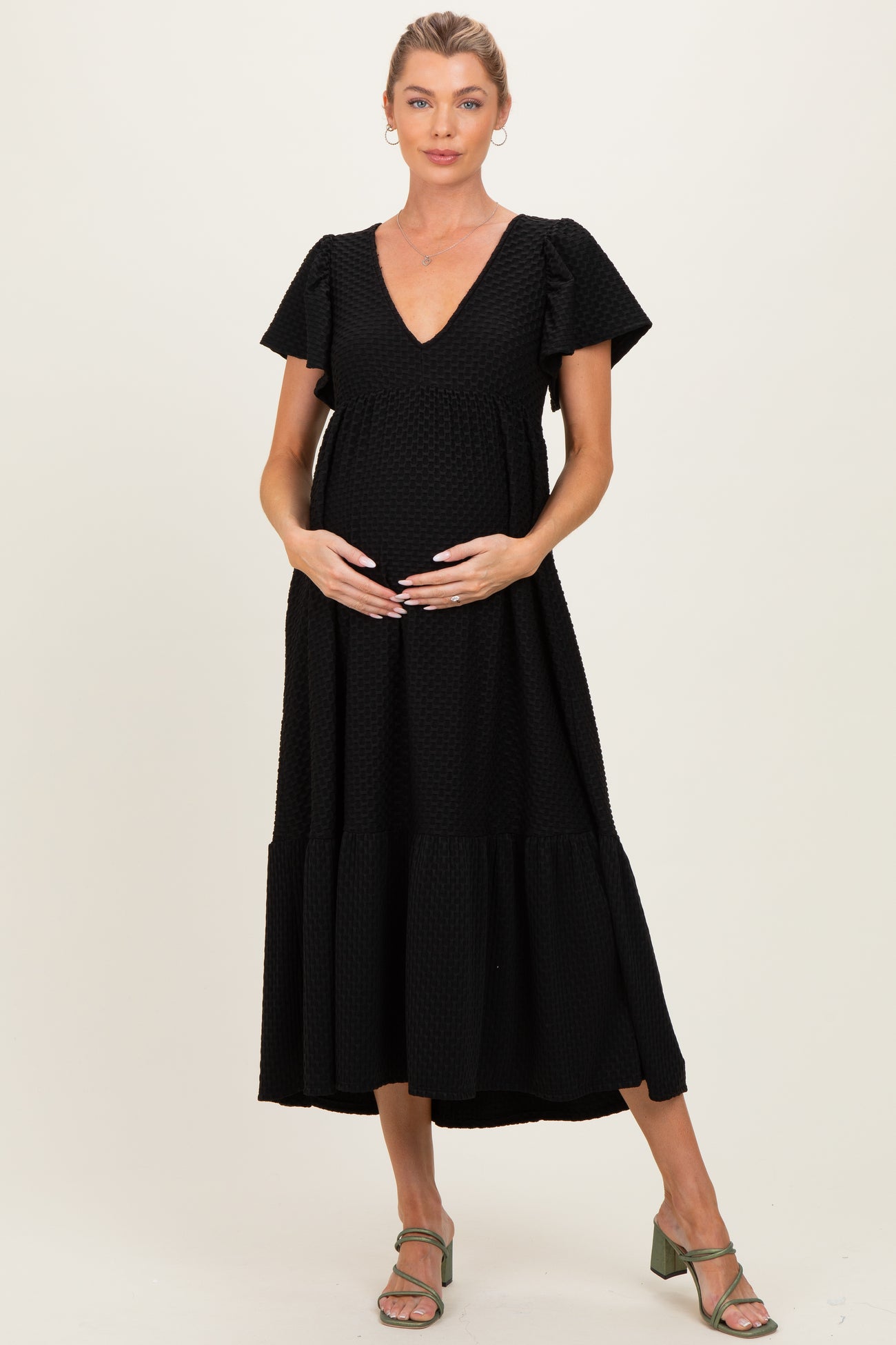 woman wearing a black maternity dress with puff sleeves and a tiered skirt, gently cradling her baby bump