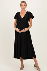 woman wearing a black maternity dress with puff sleeves and a tiered skirt, gently cradling her baby bump